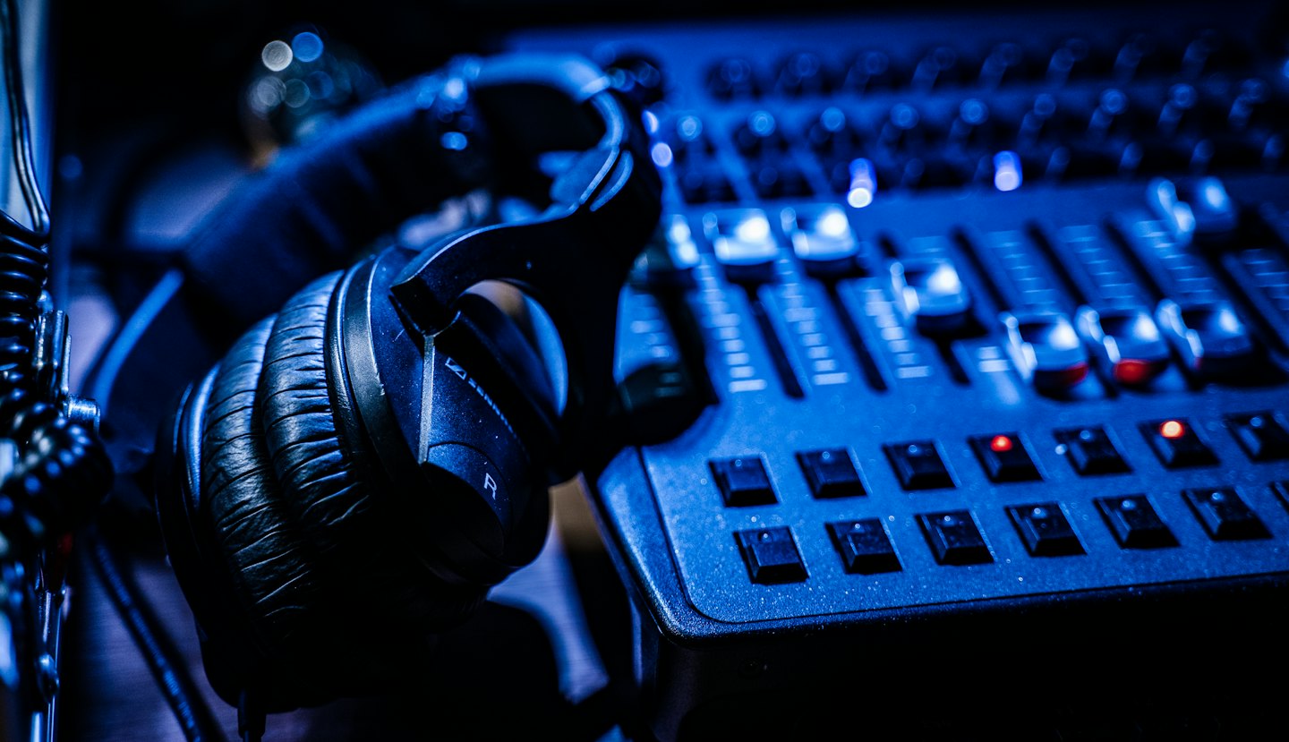 Cuffie nere su una console di missaggio audio con luce blu.