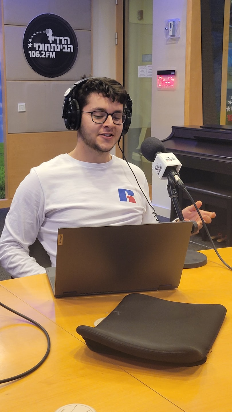 Uomo con occhiali e cuffie parla in un microfono da studio.